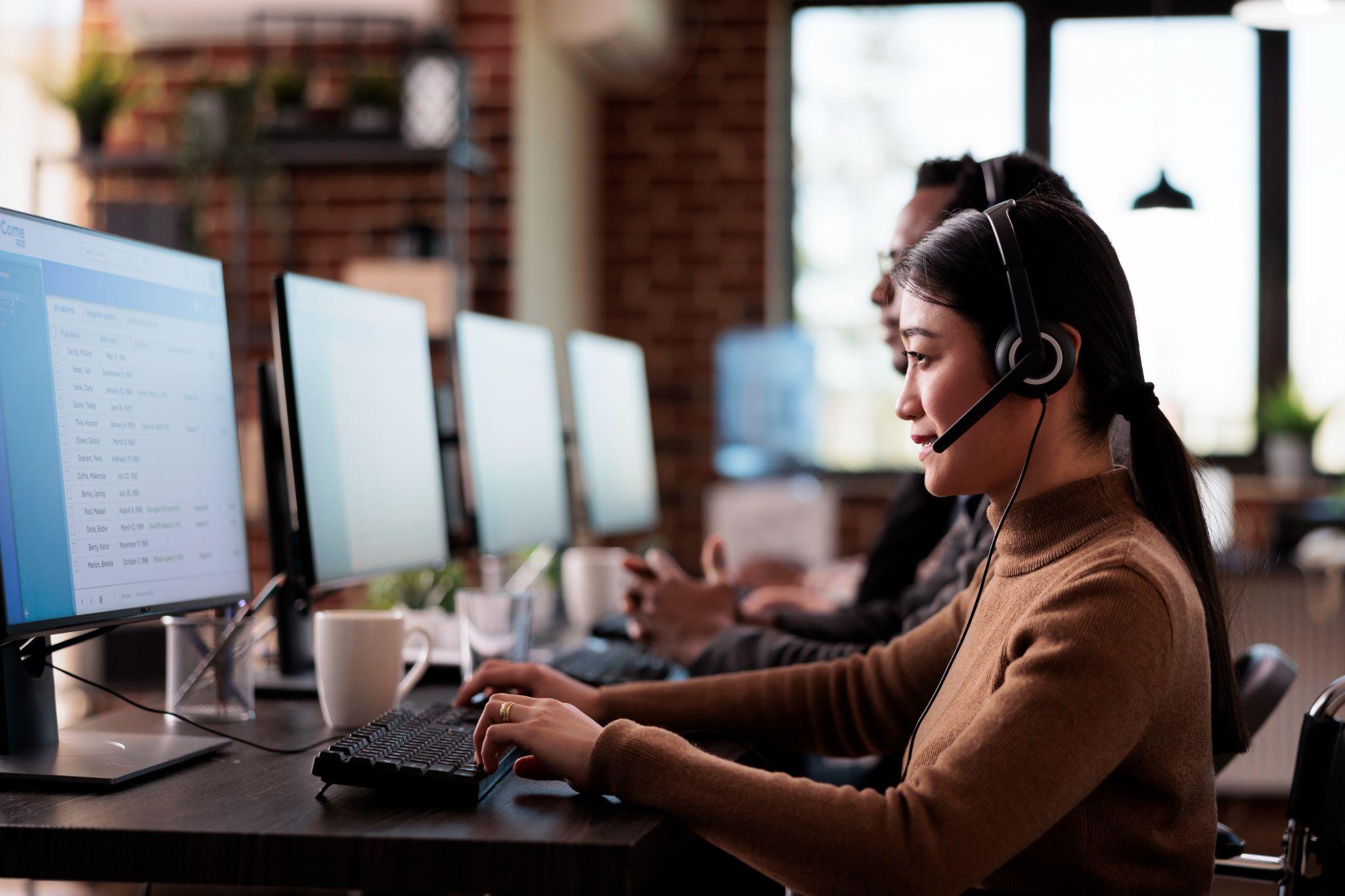 A customer service representative wearing a headset and working at a computer in an office setting