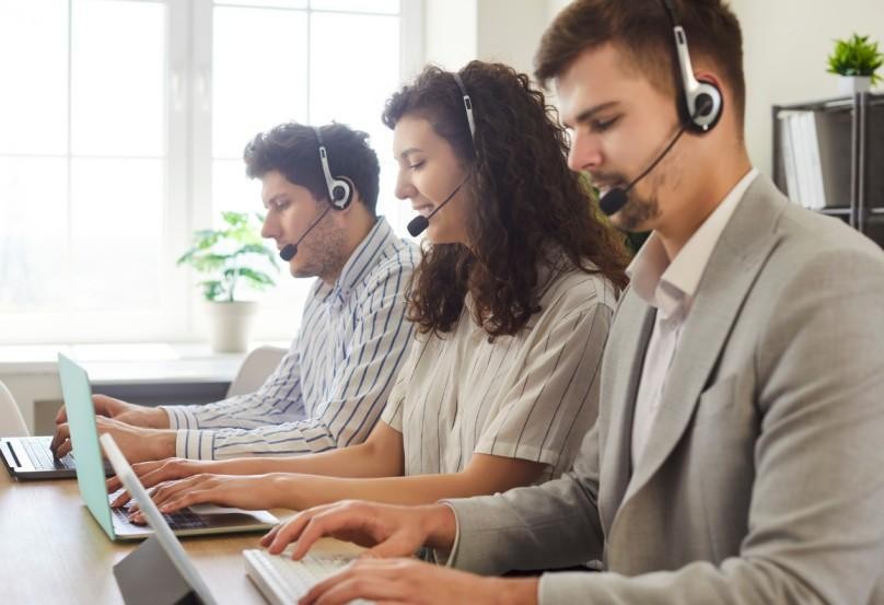 Three customer support agents wearing headsets and working on laptops in an office setting
