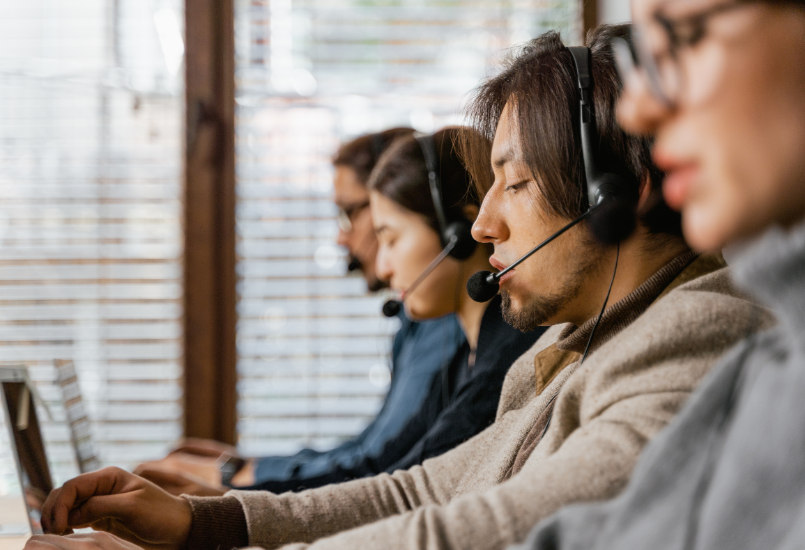 A group of customer service representatives wearing headsets and working at computers in an office setting
