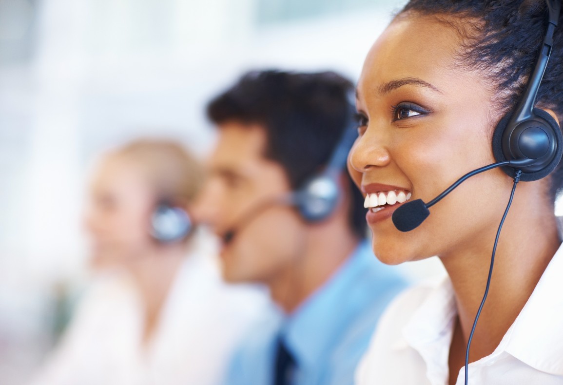 A group of customer service agents wearing headsets and smiling while working at their desks