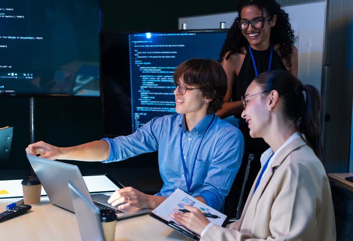 Three colleagues collaborating in a modern office with computer screens displaying code in the background